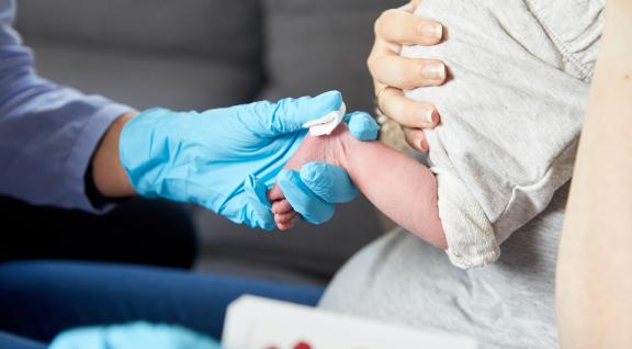 Zorgverlener neemt bloed af voor de hielprik bij een pasgeboren baby