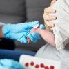 Zorgverlener neemt bloed af voor de hielprik bij een pasgeboren baby
